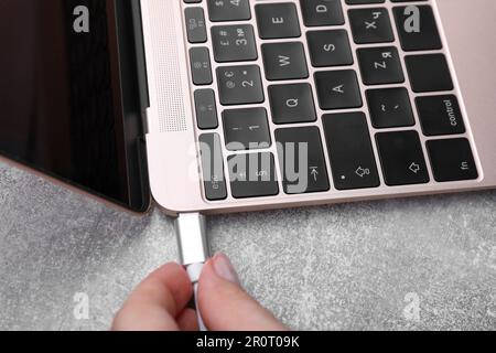 Donna che inserisce il cavo USB nella porta del computer portatile al tavolo grigio, primo piano Foto Stock