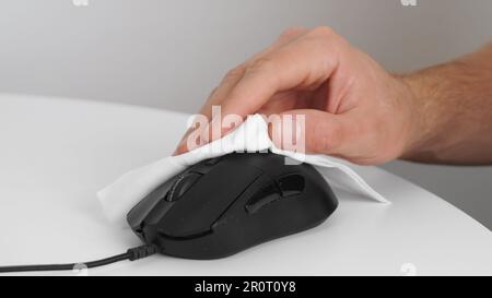 Uomo pulizia computer mouse con salvietta disinfettante al tavolo bianco in ambienti chiusi, primo piano. Misure di protezione Foto Stock