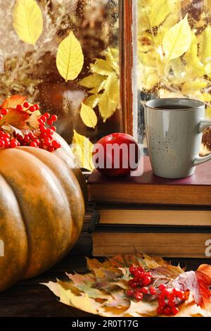 Pila di libri, tazza con tè aromatico, zucca e foglie secche sul davanzale in legno all'interno. Atmosfera autunnale Foto Stock