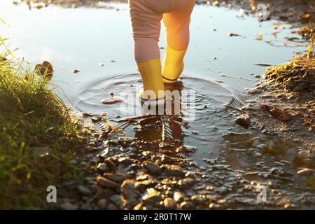 Bambina che indossa stivali di gomma camminando in pozza all'aperto, primo piano Foto Stock