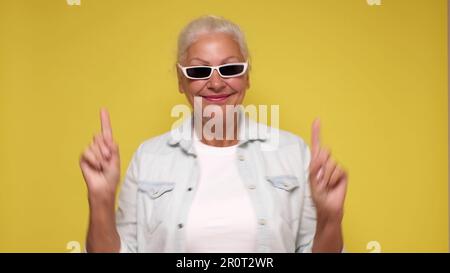 Una donna anziana punta il dito per attirare l'attenzione su uno sfondo beige Foto Stock
