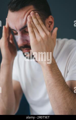 Primo piano ritratto di un uomo, seduto a casa sul divano nel soggiorno con gli occhi chiusi, soffriva di mal di testa, massaggiando le tempie. Primo piano Foto Stock