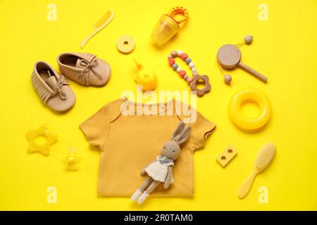 Composizione con abiti per bambini, giocattoli e accessori su sfondo giallo Foto Stock