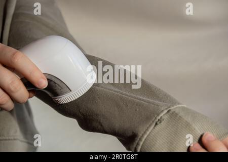Donna che usa un rasoio Anti-pilling a casa. Dispositivo per la rasatura di indumenti in pellet. Rasoio in tessuto anti-peluche. Pulitore elettrico portatile pillola defuzzer pelucchi da acrilico o lana maglione. Sostenibilità stile di vita, riducendo il riciclaggio dei rifiuti di abbigliamento Foto Stock