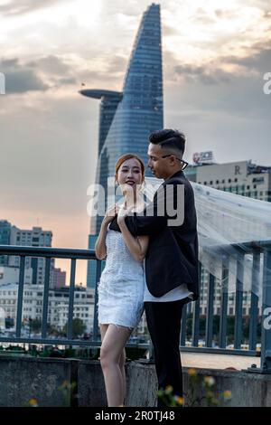 Coppia di nozze vietnamita in posa per fotografie di fronte allo skyline della città di ho Chi Minh sul fiume Saigon, Vietnam Foto Stock