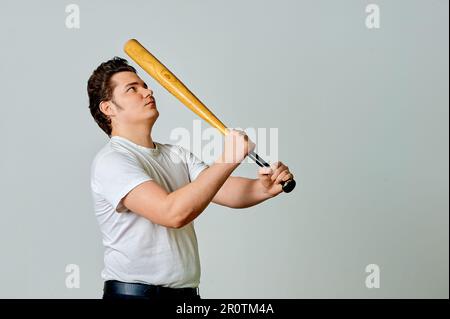 Un uomo con un pipistrello in mano oscilla su uno sfondo grigio Foto Stock
