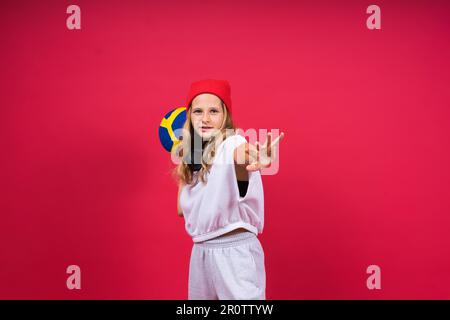 Una ragazza adolescente tiene la palla da pallavolo in mano e sorride su sfondo giallo rosso. Foto studio. Foto Stock