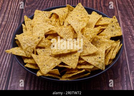 Nachos in una ciotola nera. Tortilla chip su sfondo di legno. Foto Stock