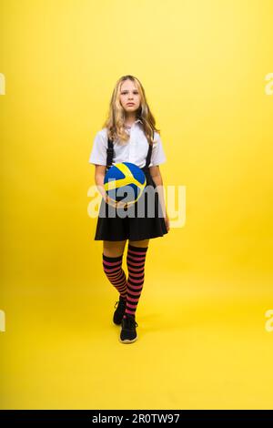 Una ragazza adolescente tiene la palla da pallavolo in mano e sorride su sfondo giallo rosso. Foto studio. Foto Stock
