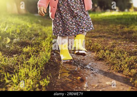 Bambina che indossa stivali di gomma camminando in pozza all'aperto, primo piano Foto Stock