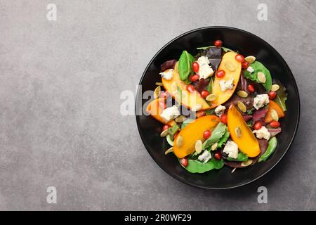 Deliziosa insalata di persimmon con melograno e spinaci su sfondo grigio chiaro, vista dall'alto. Spazio per il testo Foto Stock