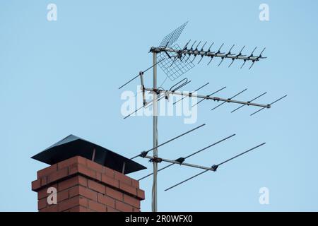 Antenna TV sul tetto rosso. antenna televisiva sul tetto con cielo blu. Tubo di mattoni casa e media trasmettitore, radio, televisione Foto Stock