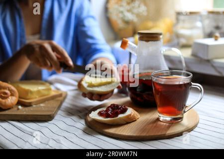 Donna che spalma il burro sul pane al tavolo al coperto, concentrarsi sul tè aromatico Foto Stock