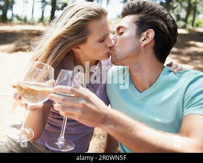 Tostare al loro amore. Vista laterale di una bella giovane coppia che bacia e ha champagne all'aperto. Foto Stock