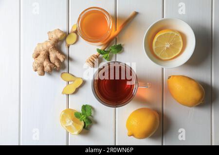 Tazza di delizioso tè allo zenzero, miele e limoni su un tavolo di legno bianco, piatto Foto Stock