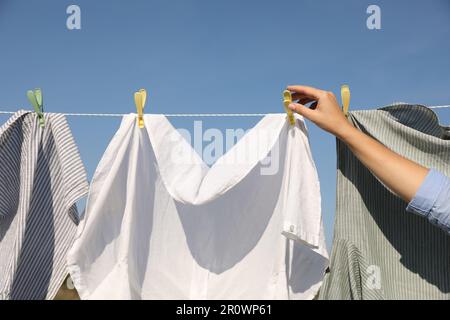 Donna appendere abiti con clothespins sulla linea di lavaggio per asciugare sotto cielo blu all'aperto, primo piano Foto Stock