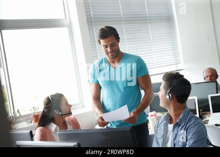 Piacevolmente impressionato dalla loro prestazione. Un bell'uomo in piedi in un ufficio e che tiene un rapporto di ufficio mentre i colleghi sono seduti alla scrivania Foto Stock