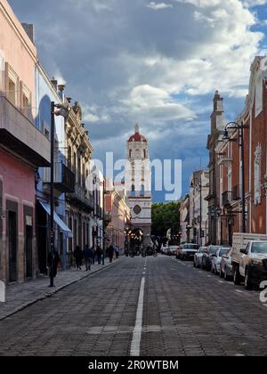 Una strada cittadina con edifici su entrambi i lati, piena di pedoni che camminano nel tempo nuvoloso. Foto Stock