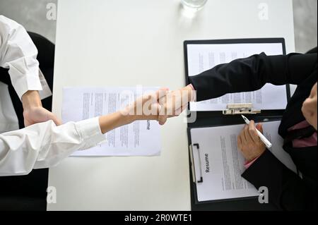 Vista dall'alto di una donna professionista senior reclutatore o di una donna d'affari che scuote le mani con un giovane candidato maschile dopo un colloquio di lavoro. Foto Stock