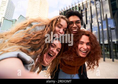 Gruppo di studenti amici divertirsi all'aperto prendendo un selfie guardando la fotocamera mentre si fa piggyback Foto Stock