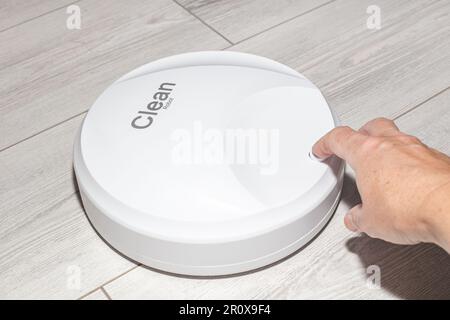 una donna accende un aspirapolvere robot su una borsa bianca. Assistenti intelligenti per la pulizia della casa. Foto Stock