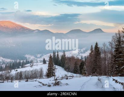 Sunrise mattina inverno villaggio montano di periferia in nero Cheremosh river valley tra alp. Vista dalla campagna coperta di neve percorso sul versante collinare con ch Foto Stock