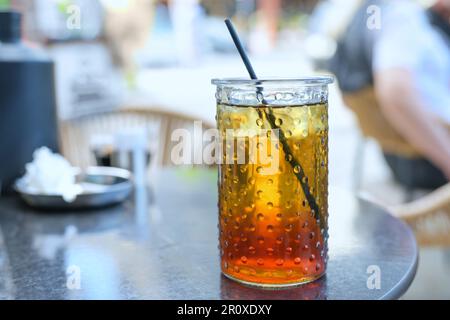 Tè freddo rinfrescante con sciroppo di limone e una cannuccia bevente in un bicchiere in un caffè di strada in estate, focus selezionato, profondità di campo stretta Foto Stock