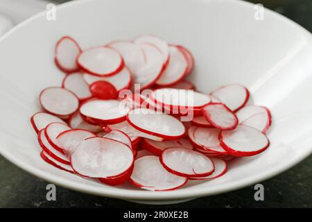 Fette di ravanello fresco crudo in una ciotola bianca, spazio di copia, messa a fuoco selezionata, profondità di campo ridotta Foto Stock