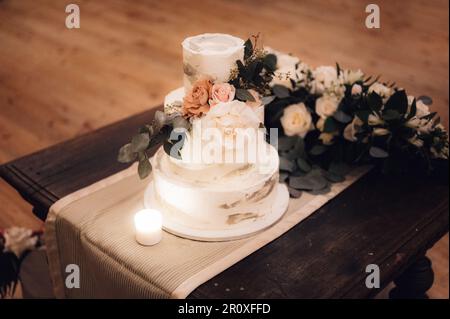 Torta a tre livelli con fiori freschi sistemata su un tavolo di legno in una stanza con pavimento in legno Foto Stock