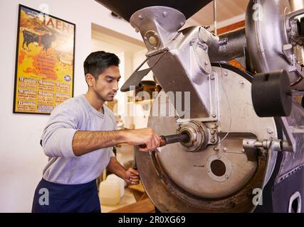 Perfezionare il suo processo di tostatura. una macchina per macinare e tostare i chicchi di caffè. Foto Stock