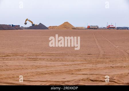 Macchine per la costruzione e il sottopiede di sabbia, cumuli di sabbia e ghiaia sullo sfondo. Cantiere stradale. Foto Stock