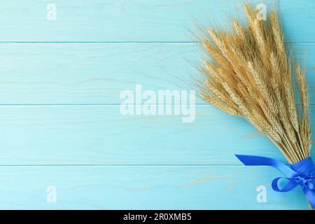 Shavuot festa ebraica. Bouquet di grano maturo dorato con nastro blu. Tavola in legno bianco con campo di grano. Sfondo per Shavuot Foto Stock