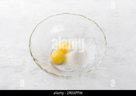 Ciotola di vetro con zucchero e due tuorli su fondo grigio chiaro. Impastare per biscotti fatti in casa Foto Stock