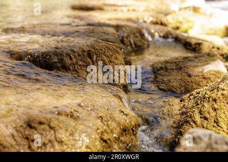 Primo piano di acqua fresca che scorre sulle rocce alla luce del sole, creando un'idilliaca scena naturale Foto Stock