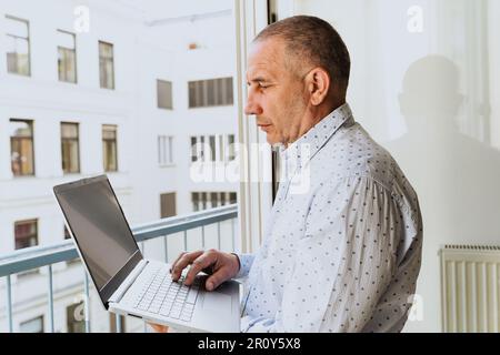 Uomo attraente in camicia in piedi vicino alla finestra con il laptop Foto Stock