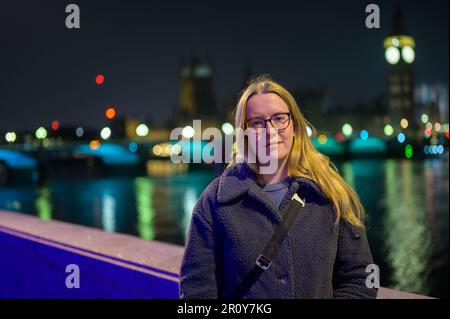 Donna bionda in posa di fronte alle case illuminate del Parlamento di notte. Foto Stock