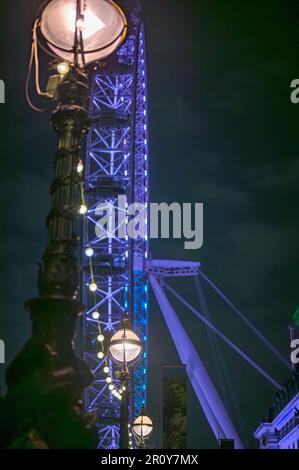 LONDRA - 21 aprile 2023: Un London Eye blu si illumina sullo sfondo mentre le luci della strada illuminano la passeggiata della Regina di notte. Foto Stock