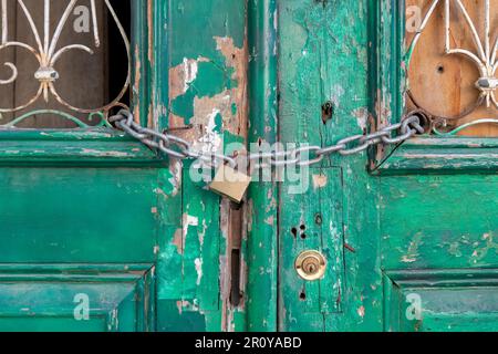 Vista ravvicinata delle vecchie porte doppie dipinte di verde con sbucciatura della vernice e trucioli di legno con asse dietro ornamenti in ferro all'apertura della porta Foto Stock