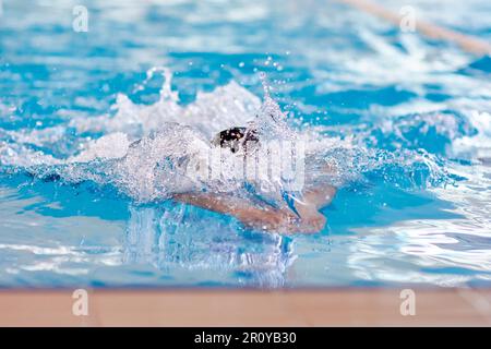 un nuotatore di beanie allunga le braccia in acqua durante un allenamento al seno in piscina, sfocato Foto Stock