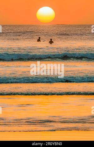 I surfisti aspettano onde al tramonto sulla spiaggia di Guiones, in questa popolare destinazione di hip surf e yoga. Playa Guiones, Nosara, Nicoya, Guanacaste, Costa Rica Foto Stock