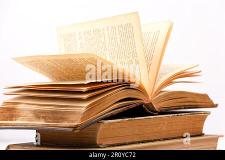 vecchio libro aperto vintage con alcune pagine visibili che giacciono sopra altri libri con sfondo bianco Foto Stock