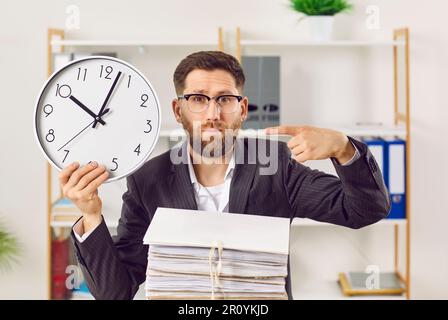 Ritratto dell'uomo d'affari che punta con il dito a un grande orologio da parete Foto Stock