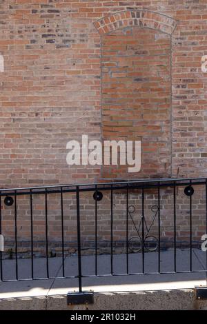 Primo piano texture sfondo di un vecchio muro di mattoni fiammato e chic, con vista su un'antica finestra ad arco e una recinzione di ferro Foto Stock