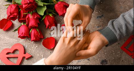 Uomo che mette l'anello di fidanzamento sul dito della donna contro lo sfondo grunge Foto Stock