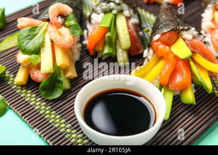 Stuoia di bambù con gustosi coni di sushi e salsa di soia su sfondo colorato, primo piano Foto Stock