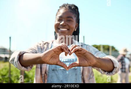 Ritratto di un coltivatore felice. Giovane contadino che crea una forma di cuore con le mani. Contadino afroamericano che mostra amore. Contadino in piedi nel suo giardino Foto Stock