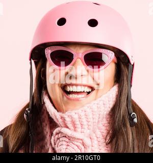 Stare giovani a cuore. una donna matura in piedi da sola in studio mentre indossa occhiali da sole e un casco. Foto Stock