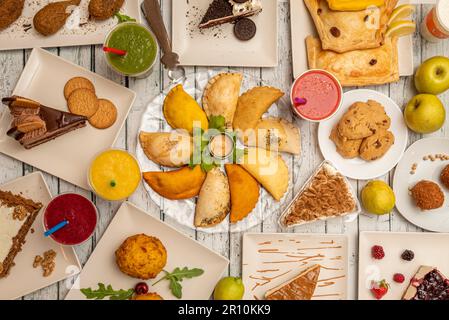 Una serie di sostanziosi piatti latini con empanadas assortiti, dessert e patate farcite Foto Stock