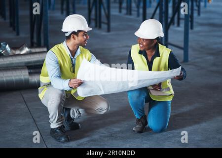 So che potete farlo. due giovani appaltatori accovacciati nel magazzino insieme e utilizzando un modello per pianificare. Foto Stock