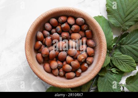 Gustose nocciole in ciotola di legno e ramo su tavolo di marmo chiaro, piatto Foto Stock